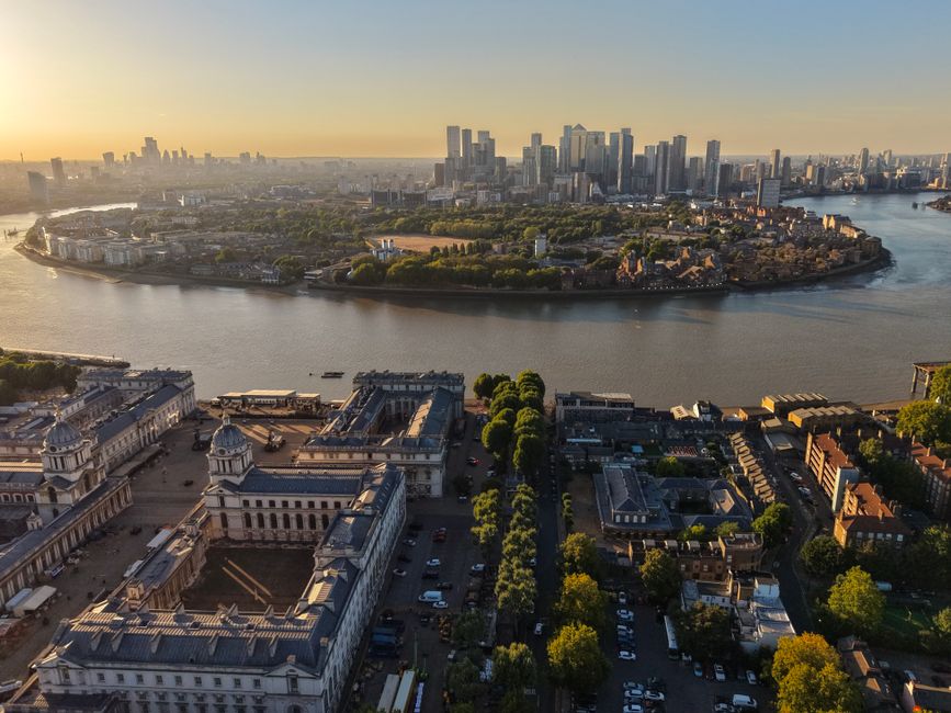 An aerial view taken during the late afternoon or early evening showing the cityscape of Greenwich in London, with a wide river flowing through the area. In the foreground, there are historic building