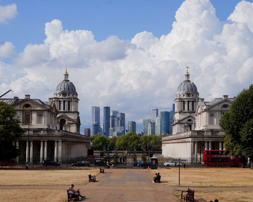 An aerial view taken during the late afternoon or early evening showing the cityscape of Greenwich in London, with a wide river flowing through the area. In the foreground, there are historic building